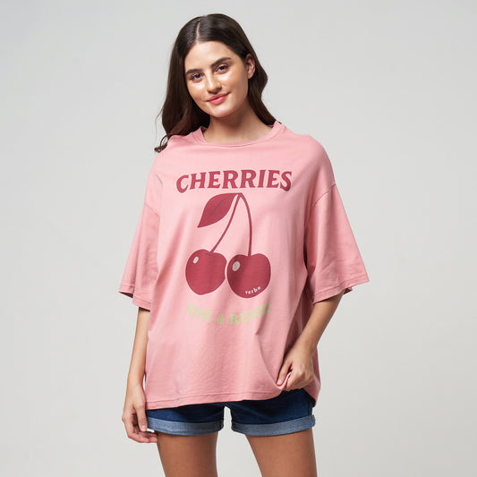 Female Model wearing the Rose Tan Cherries tee in a lifestyle studio setting, highlighting of the boxy fit.