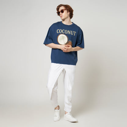 Male model styled in the VERBO Coconut Boxy Oversized Tee in Stargazer blue with white wrap trousers and sunglasses.