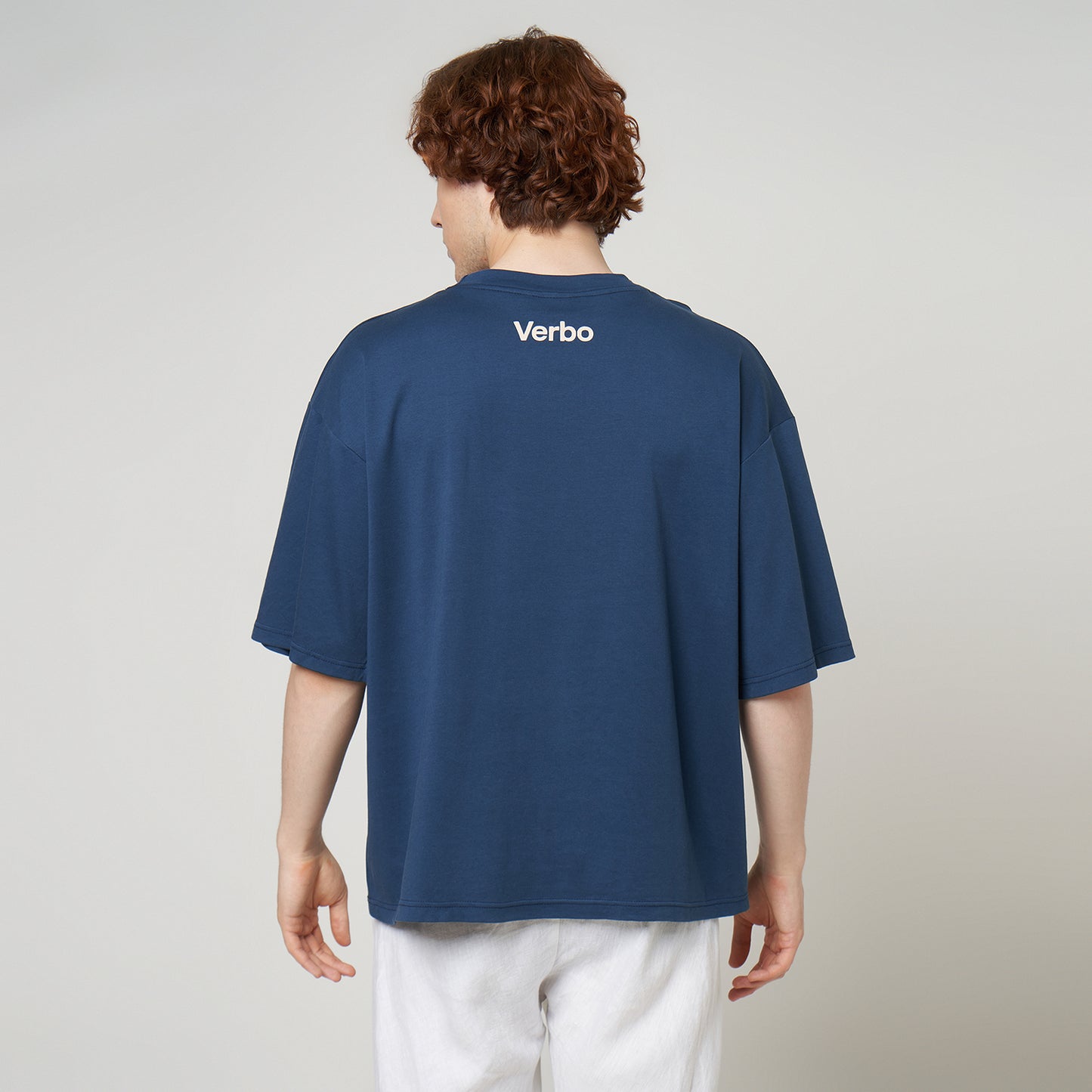 Model wearing the VERBO oversized tee from behind, showcasing the loose silhouette and high-neck "Verbo" branding.