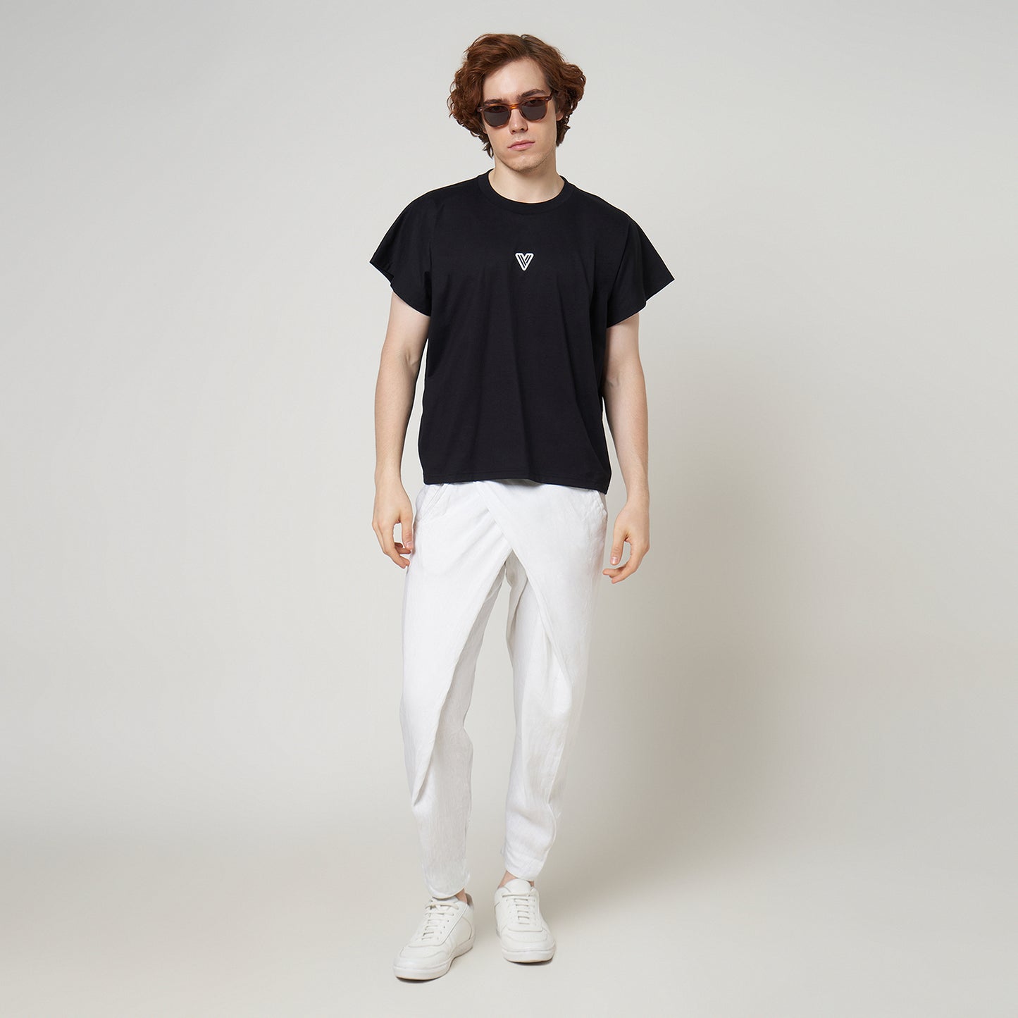 Male model wearing the VERBO Noir black cropped tank with white linen trousers for a modern minimalist streetwear look.