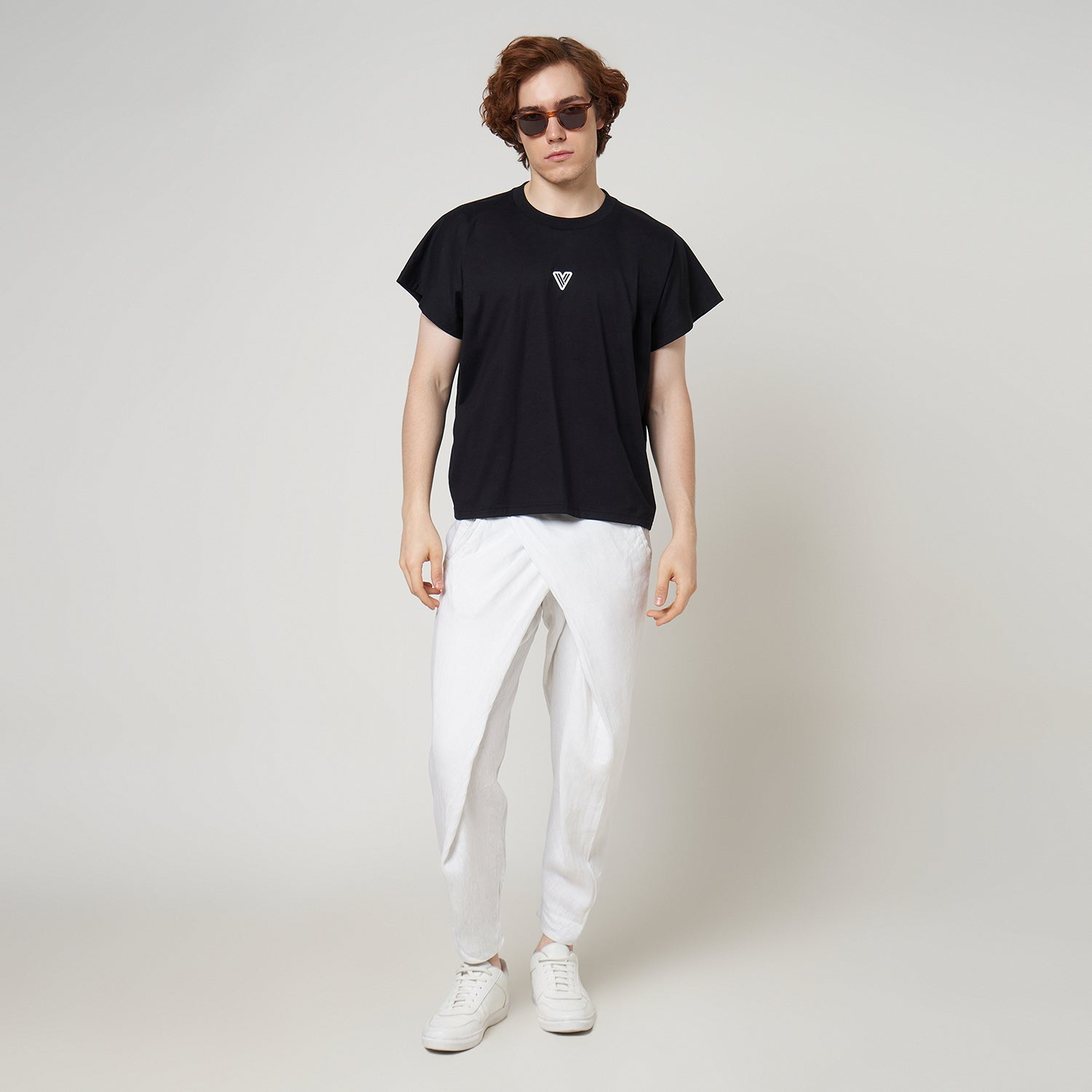 Male model wearing the VERBO Noir black cropped tank with white linen trousers for a modern minimalist streetwear look.