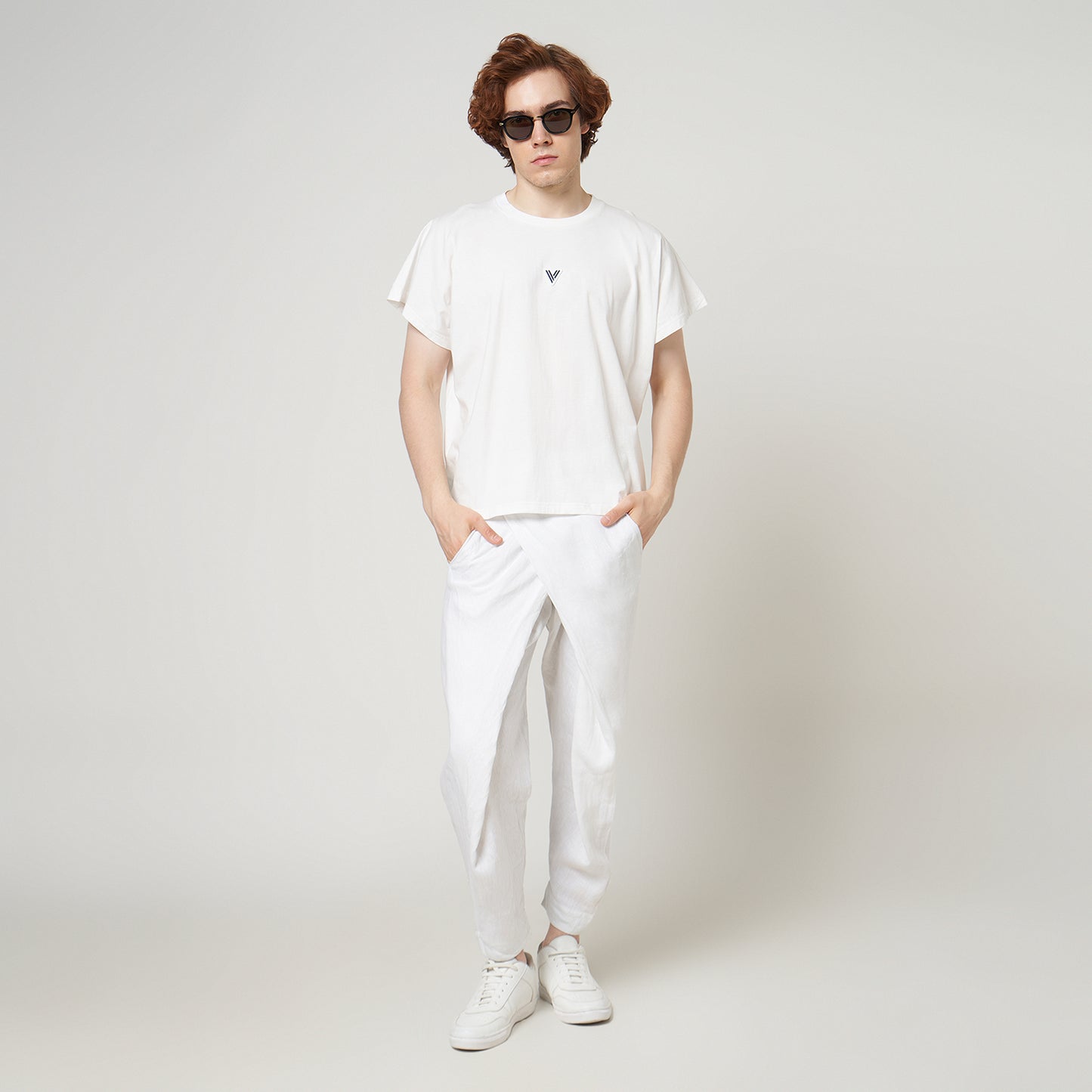 Male model wearing the VERBO white cropped tank with white linen trousers for a modern minimalist streetwear look.