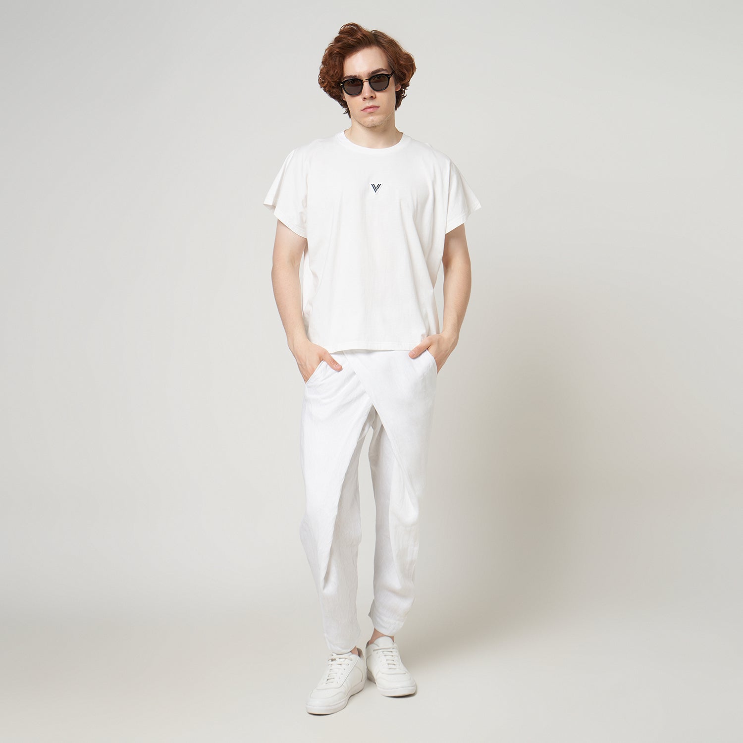 Male model wearing the VERBO white cropped tank with white linen trousers for a modern minimalist streetwear look.