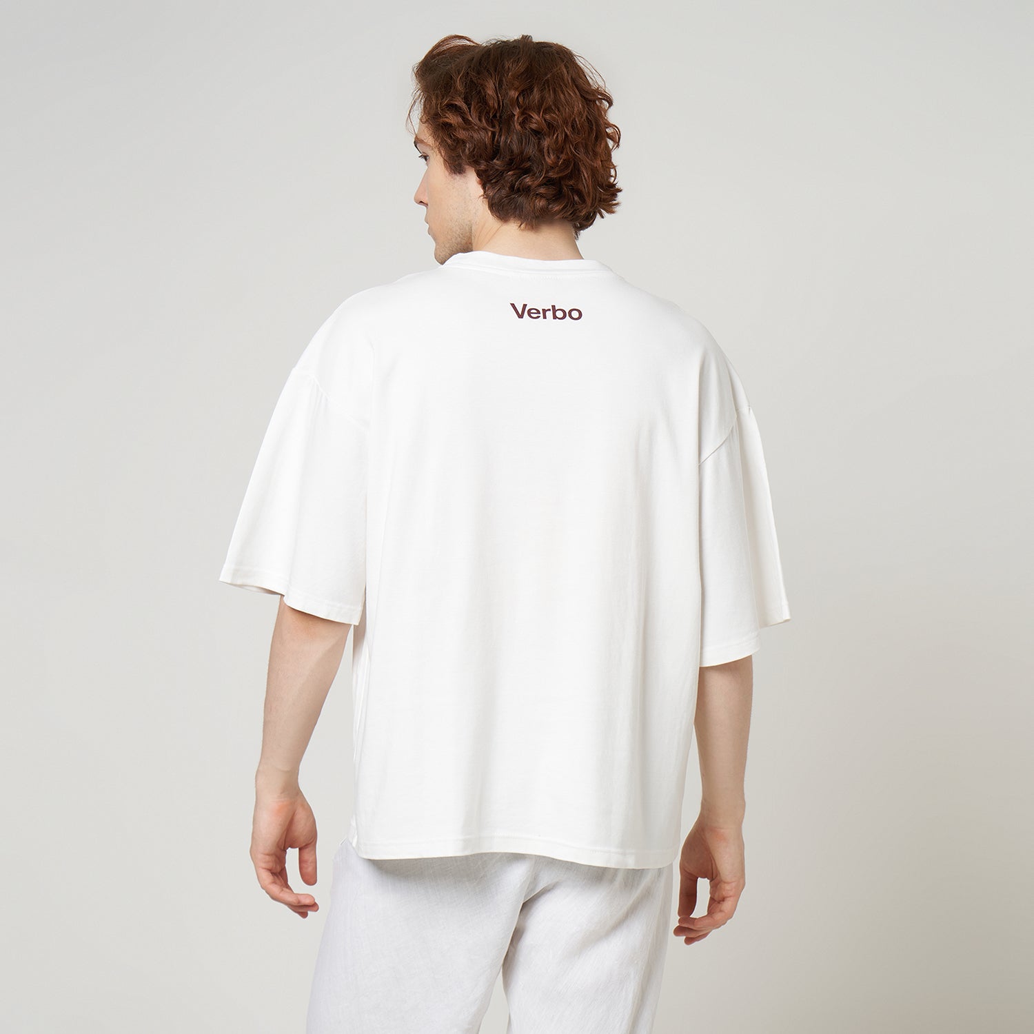 Model showcasing the wide, oversized fit and back branding of the VERBO Broken White Apple Tee.