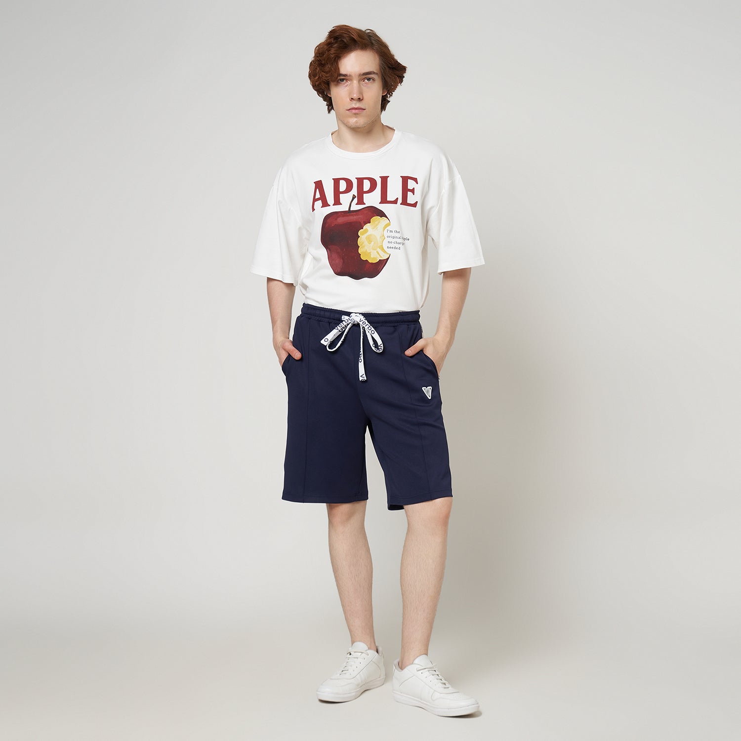 Person wearing a white t-shirt with an apple graphic and navy shorts on a plain background