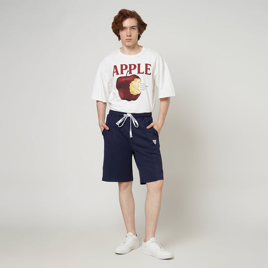 Person wearing a white t-shirt with an apple graphic and navy shorts on a plain background